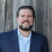 headshot of AtlasIED General Manager Justin Young leaning on wood background